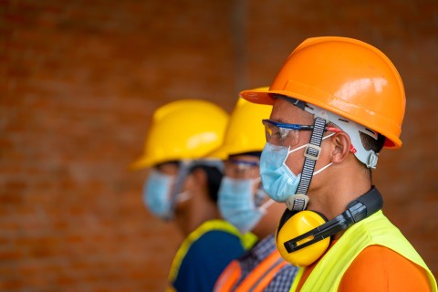 Side view of three men standing and wearing PPE